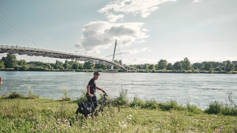 Jobradler schiebt sein Rad in einer Blumenwiese am Flussufer