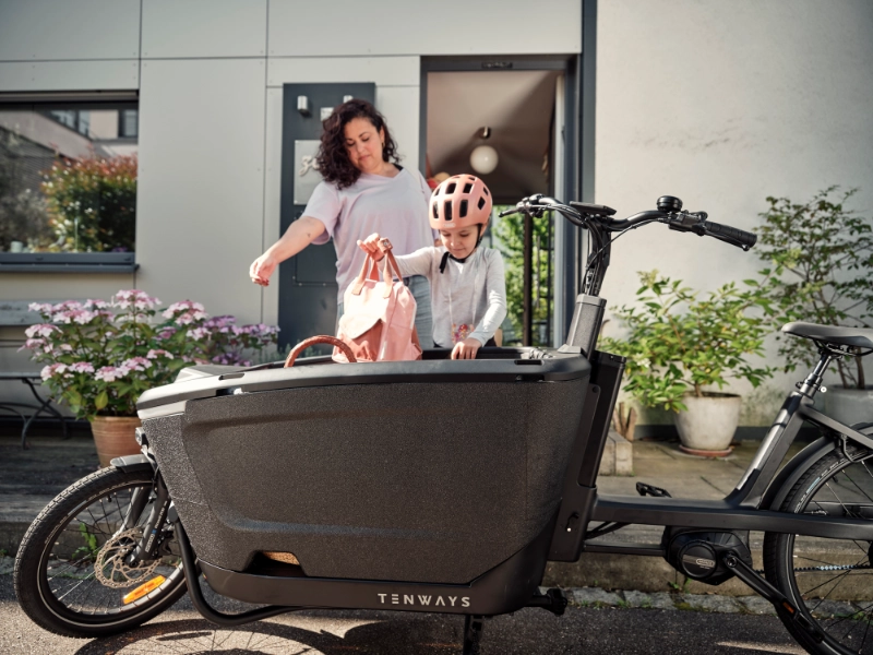 Alltagsszene: Frau und Kind kommen aus der Haustüre und beladen ein Lastenfahrrad.