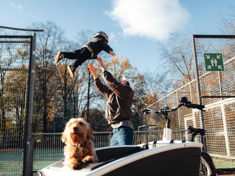 Vater wirft seinen Sohn in die Luft, im Vordergrund Hund