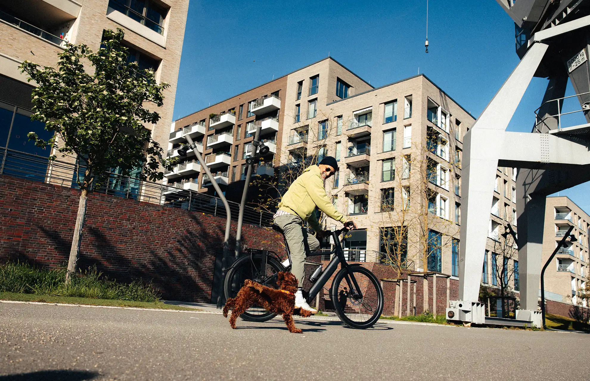 Junger Mann fährt in städtischer Umgebung Fahrrad, kleiner brauner Hund an der Seite